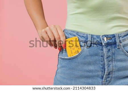 Close up cropped young woman 20s years old wears mint t-shirt jeans hold in pocket credit bank card isolated on plain pastel light pink background studio portrait. Achievement career wealth concept