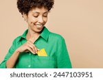 Close up cropped young woman of African American ethnicity wear green shirt casual clothes hold in hand put mock up of credit bank card into pocket isolated on plain beige background Lifestyle concept