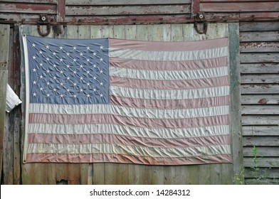 Close cropping of a faded American flag hanging from the side of an old red shack in Upstate New York.