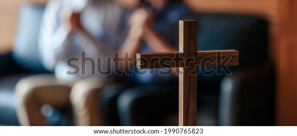 Close\
up cross is blur background. Asian Christian woman and man holding\
hands in praying for Jesus\' blessings to show love and confession\
of their sins according. Concept giving love\
faith