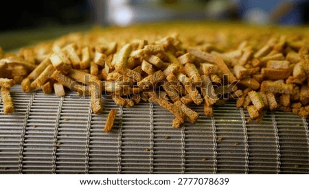 Close up of croutons or bread snacks moving quickly along a metal conveyor belt in a food factory. The automated machinery processes and sorts the baked goods in a continuous stream