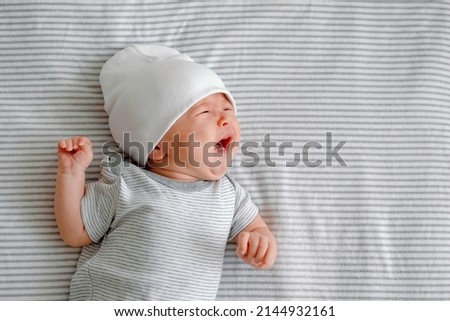 Close up of a crying newborn laying on a striped gray nappy. Hangry baby. Infantile colic. Baby care