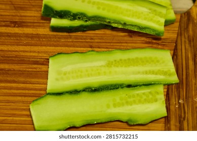 close up of a cucumber cut into thin slices to be used for a hamburger on a wooden chopping board