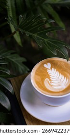 Close up of a cup of latte with leaf pattern latte art and green leaves background