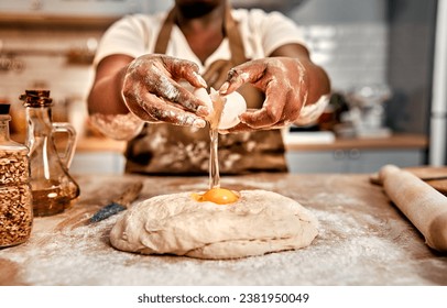 Close up of curvy afro woman in apron cracking raw egg into dough during baking process at home. Wise housewife standing behind kitchen counter and working with pastry products.                        - Powered by Shutterstock