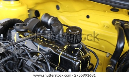 Close up of a custom modified car engine featuring a black valve cover with yellow paint splatter and an aftermarket breather filter