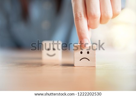 Close up customer hand choose sad face and blurred smiley face icon on wood cube, Service rating, satisfaction concept.