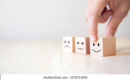 Close Up Customer Hand Choose Smiley Face And Blurred Sad Face Icon On Wood Cube, Service Rating, Satisfaction Concept.