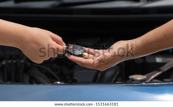 Close up of customer hand giving\
car key to car engine repairman on car engine background to repair\
it . Concept of maintenance vehicle mechanic and\
automotive