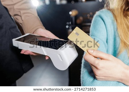 Close up of customer and waiter hands using NFC bank card with portable POS terminal for cashless checkout in bar cafe interior