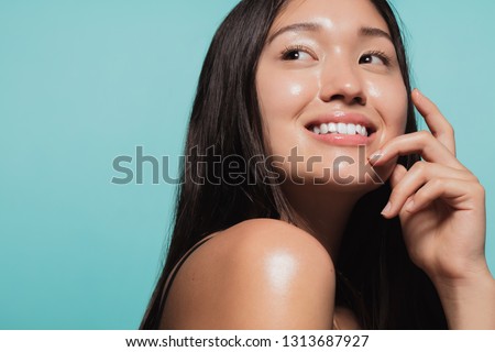 Close up of cute asian girl with glowing skin against blue background. Beautiful face of girl with fresh healthy skin.