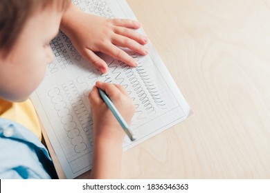 Close Up Of Cute Boy Doing His Homework. Child Writing With Pencil. Prewriting Practice To Prepare Hands For Write Letters. Children Education Concept