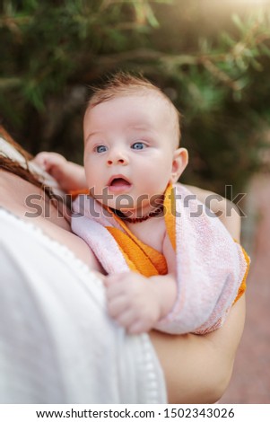 Close up of cute Caucasian 6 months old baby boy wrapped in towel after having a good time at pool. Mother holding baby.
