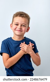 Close up of cute happy small boy isolated on white studio background hold hands at heart chest feel grateful, smiling little child pray thanking god high powers, faith concept - Shutterstock ID 2248676479