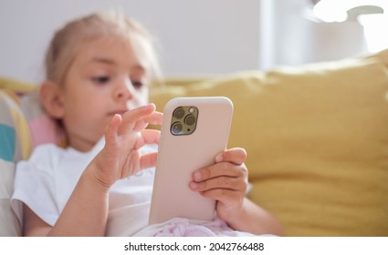 Close Up Of Cute Little 5s Caucasian Girl Child Look At Cellphone Screen Play Online Game On Gadget.Kid Using Smart Phone At Living Room.