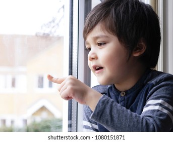 Close Up Cute Little Boy Using His Finger Drawing Or Writing On Window Glass, Adorable Kid Sitting Next To Window Waiting For Some One Back Home, Side View Of Child Handrawning On Glass.