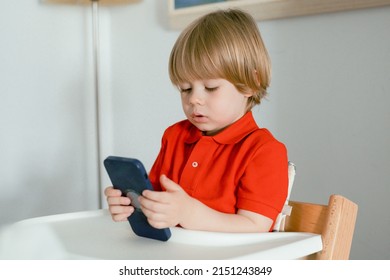 Close Up Cute Little Boy Using Smartphone, Looking At Screen, Curious Child Holding Phone In Hands, Sitting On Chair At Home Alone, Playing Mobile Device Game, Watching Cartoons Online, Chatting