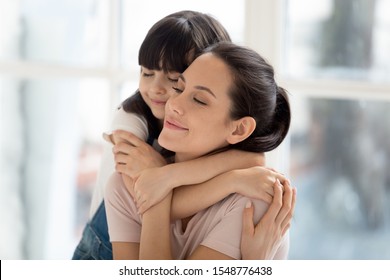 Close Up Of Cute Little Girl Hug From Behind Smiling Young Mom Showing Love And Affection, Caring Small Preschooler Daughter Embrace Cuddle Happy Mother Parent, Enjoy Tender Moment Together