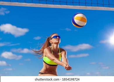 Close up of cute sexy girl passes a ball through the net while playing beach volleyball against a bright blue sky