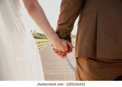 Close Up Of Cute Young Newlyweds Holding Their Hands Against Calm Sea With Lighthouse