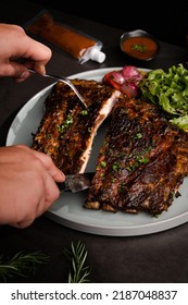 Close Up Cutting In Half Grilled Bbq Ribs By Knife In Grey Circle Ceramic Plate Om Black Table