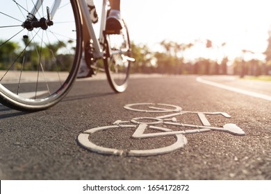 Close Up Cycling Logo Image On Road With Athletic Women Cyclist Legs Riding Mountain Bike In Background At The Morning.