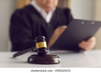 Close Up Of A Dark Brown Judge's Gavel On The Table Against The Background Of A Judge Reading The Verdict. Concept Of Justice, Law, Jurisprudence And Court Proceedings. Blurred Background.