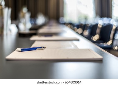 Close Up Of Dark Conference Table Water Glasses Pens, Paper Sheets And Blurry Window Background