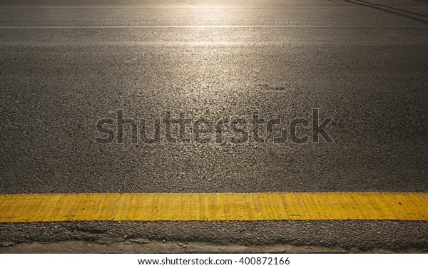 close up of a\
dark grey asphalt road divided by yellow paint  with sunshine\
reflextion selective white\
balance