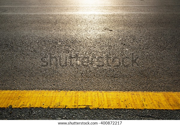 close up of a\
dark grey asphalt road divided by yellow paint  with sunshine\
reflextion selective white\
balance