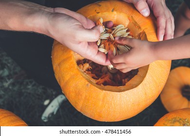 A close up of daughter and father hand who pulls seeds and fibrous material from a pumpkin before carving for Halloween. Prepares jack-o-lantern. Decoration for party. Little helper. Top view.
