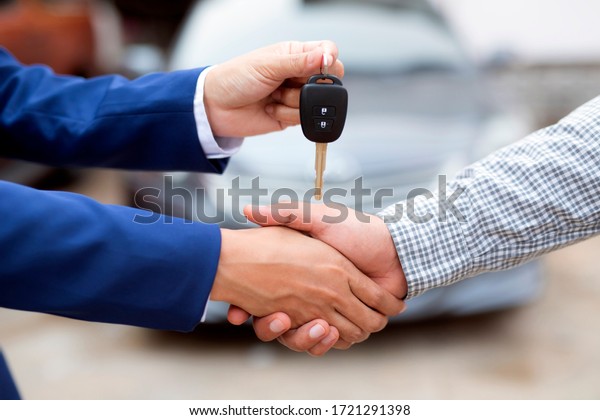 Close up of\
dealer giving key to new owner and shaking hands in auto show.auto\
business, car sale,\
deal,concept