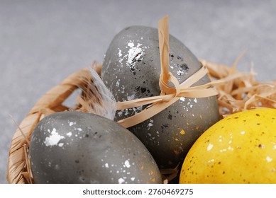 Close up decorative Easter eggs with silver speckled texture and yellow egg in wicker basket with feathers on gray background spring holiday decoration