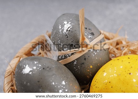 Close up decorative Easter eggs with silver speckled texture and yellow egg in wicker basket with feathers on gray background spring holiday decoration