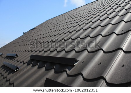 Close up of decorative metal roof and blue sky background. Grainy texture of brown metal roof tiles. Snow guard system. Ice and snow retention. Shallow depth of field