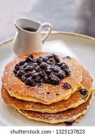 A Close Up Of Delicious Blueberry Pancakes With Maple Syrup In A Small Pitcher On A Plate With Copy Space.