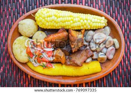 Close up of delicious hornado, ecuadorian traditional typical andean food served with corn, potato, salad, plantain and broad beans in a clay plate over a table