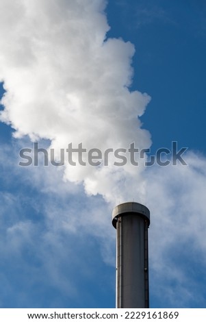 Close up of dense white smoke coming out of an industrial factory chimney against a blue sky background. Concepts of thermal energy, industry pollution and waste incineration