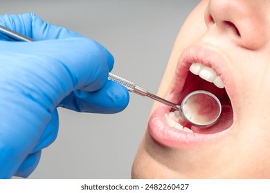 Close up of dentist hand examining patient teeth with dental mirror. - Powered by Shutterstock