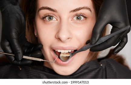 Close up of dentist hands examining woman teeth with dental mirror and explorer. Patient with open mouth while having prophylactic examination in dental clinic. Concept of dentistry and dental care. - Shutterstock ID 1999147013