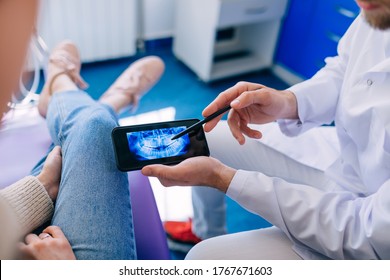 Close Up Of Dentist With Phone Showing Teeth X-ray To Female Patient. Dentist Office.