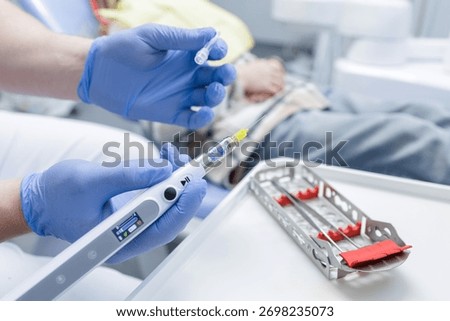 Close up of dentist preparing computer controlled anesthesia syringe with cartridge and needle for local injection in a bright dental clinic.