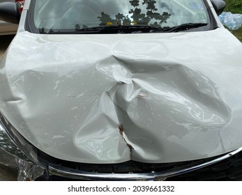 Close Up The Dents On The Car Bonnet Caused By The Accident. Front Of White Car Get Damaged By Accident On The Road.