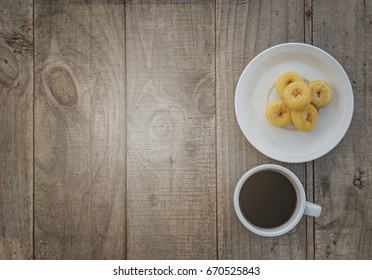 A Close Up Of A Desktop With Cup Of Coffe And Donuts On It. Wooden Background, Top View