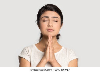 Close up of desperate hopeful young Indian woman isolated on grey studio background keep hands in prayer feel superstitious religious. Millennial mixed race female pray to God. Faith, belief concept.