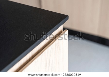 Close up detail of black stone kitchen countertop. Corner of dark gray table top surface over wooden cabinet in modern apartment with minimalist style. Scandinavian furniture in luxurious house