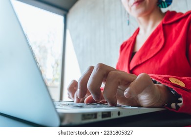 close up in detail of female fingers, of an adult caucasian woman in red clothes, typing on a laptop, sitting in a coffee shop, working on her online business.