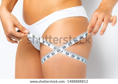 Close up detail of female hands measuring upper thigh with mesure band. Isolated on white background.