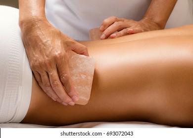 Close Up Detail Of Himalayan Salt Stone Massage. Therapist Massaging Lower Back Of Woman With Hot Salt Brick.