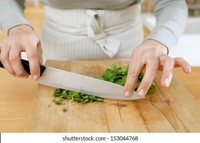 Close up detail of a middle age woman hands holding a large knife and chopping fresh green parsley on a wood chopping board in a professional kitchen, interior.